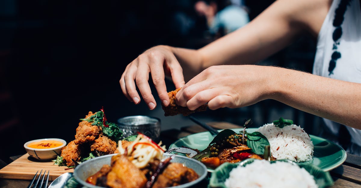 Can I carry fried rice and dried chicken preparation? - Person Holding Piece of Fried Chicken Above Plate with Food