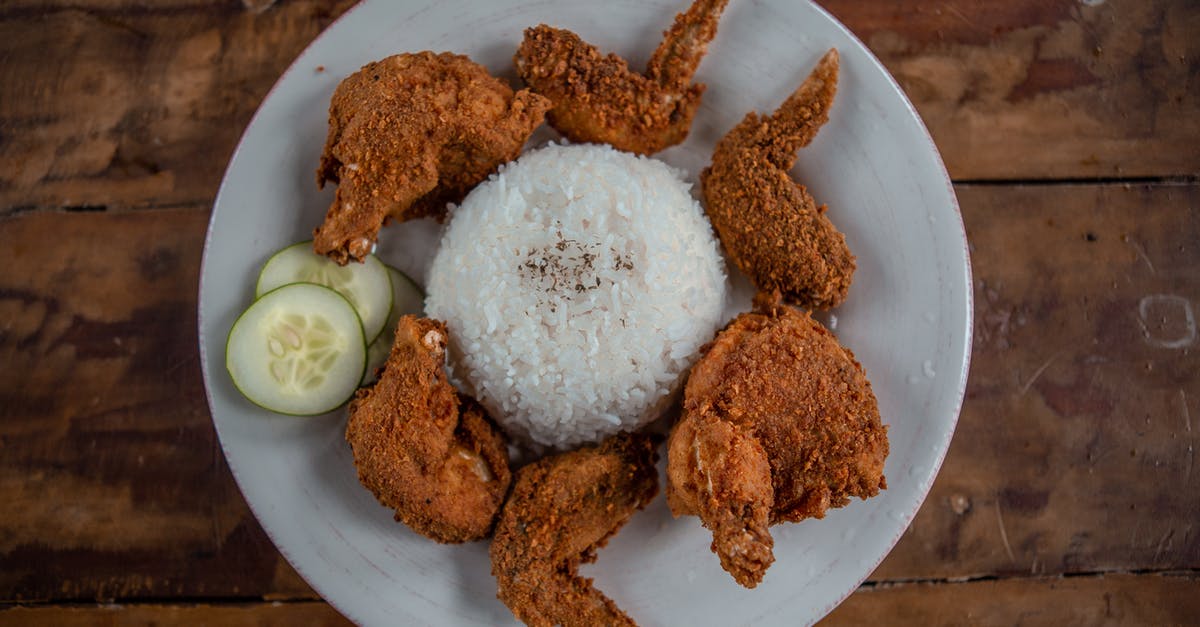 Can I carry fried rice and dried chicken preparation? - Top view of appetizing golden chicken wings with cooked rice and cucumber slices on wooden table