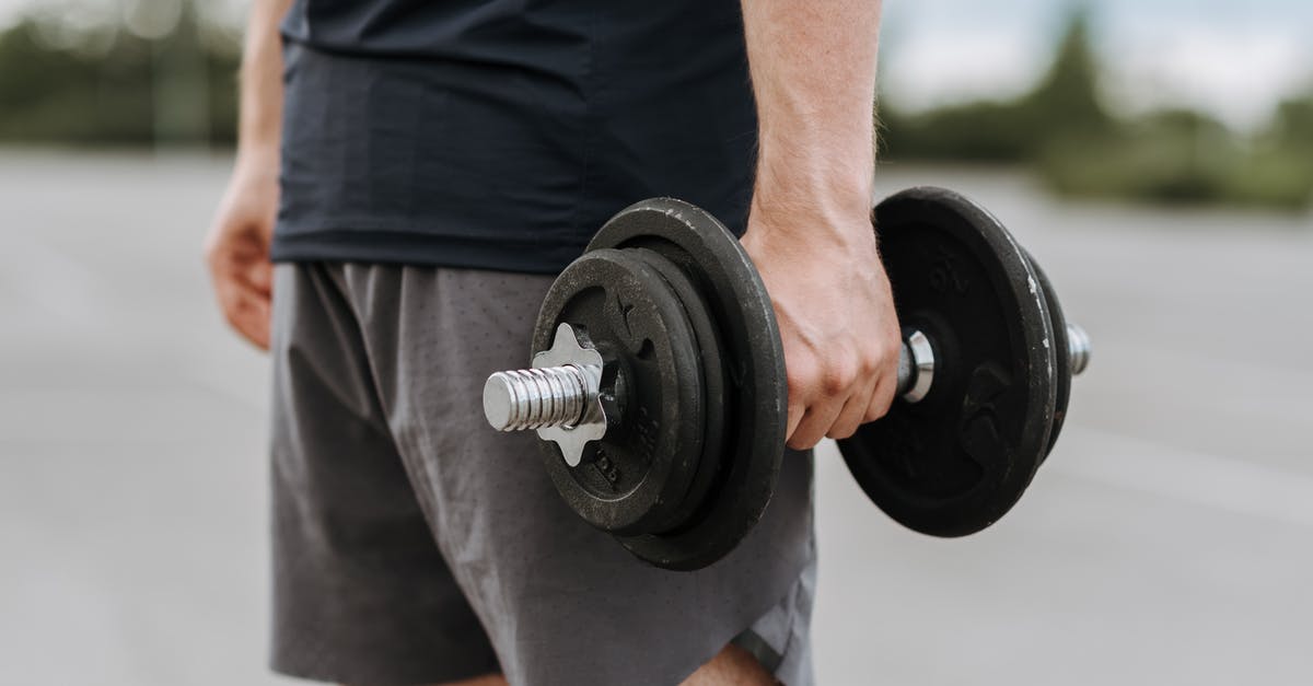 Can I carry more luggage volumes with the same weight - Crop anonymous male in activewear lifting heavy iron dumbbell on blurred background of street