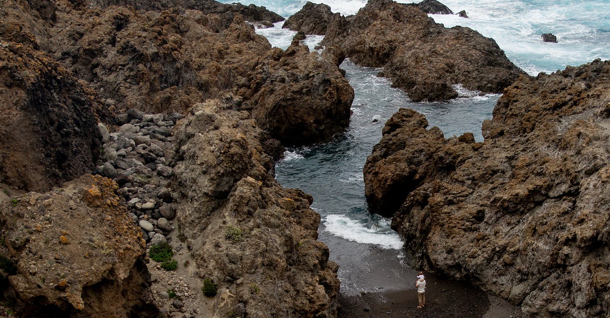 Can I carry rock climbing hardware as carry-on in Europe? - Remote back view of man carrying kid on neck while standing on rough stony coast between cliffs near waving sea during vacation