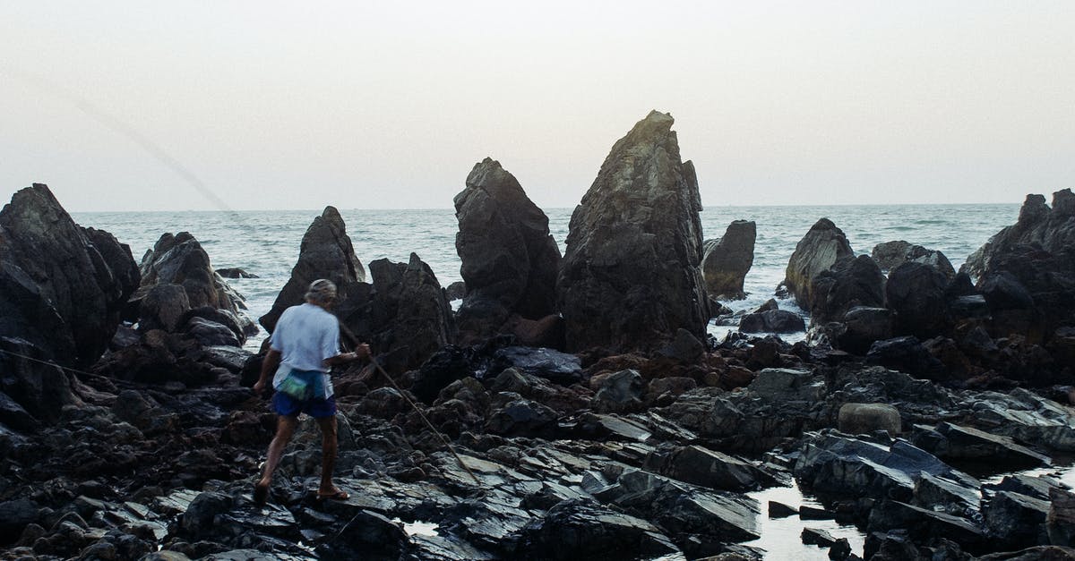 Can I carry rock climbing hardware as carry-on in Europe? - Unrecognizable fisherman with bamboo stick walking on rocky seashore