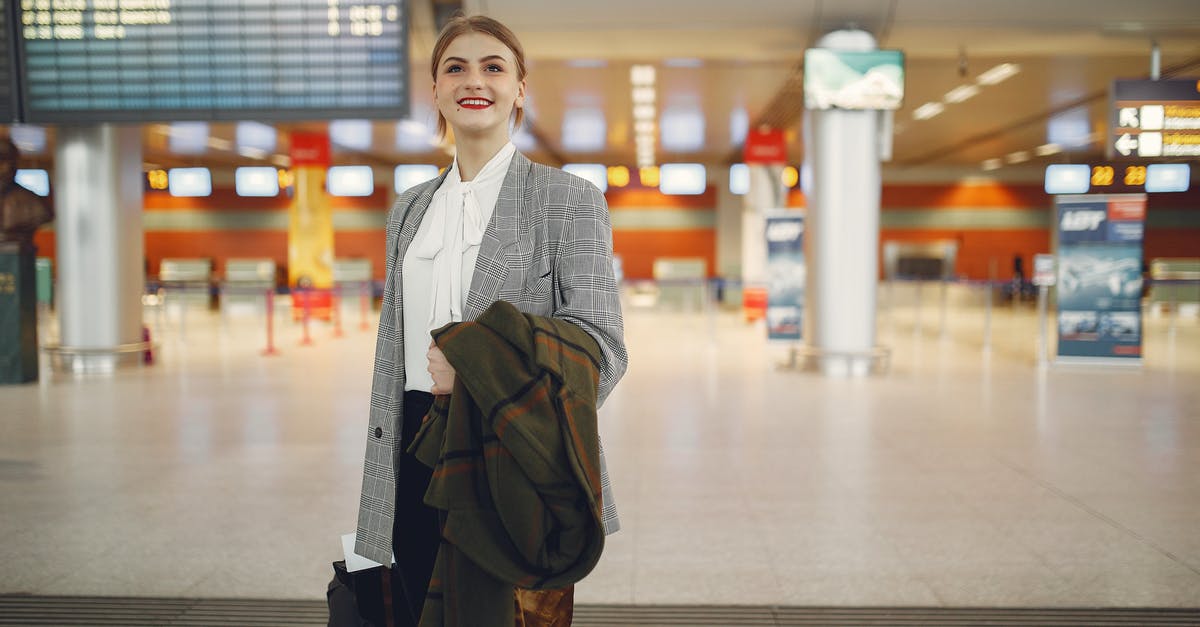 Can I check in for connecting flight in Copenhagen CPH without leaving terminal? - Happy young woman standing with baggage near departure board in airport