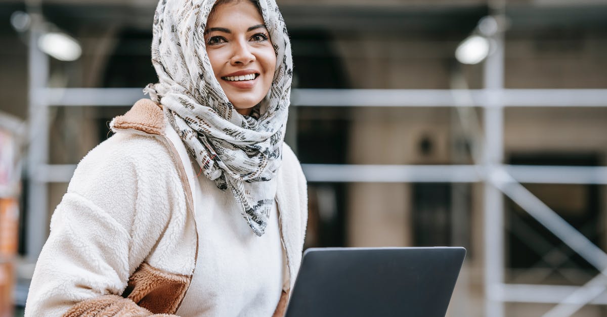 Can I communicate via an encrypted connection in United Arab Emirates? - Joyful young Arab female freelancer in casual outfit and hijab smiling while working remotely on netbook on city street