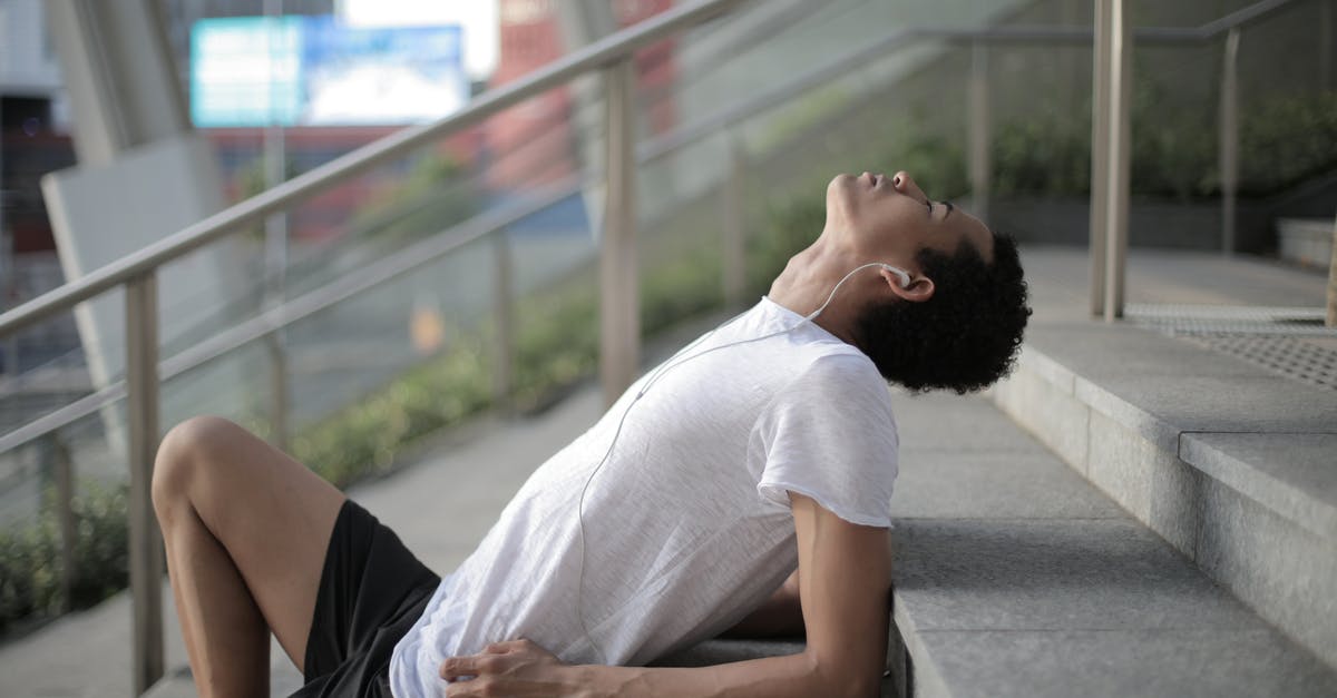 Can I dispatch luggage during a connection? - Side view of serene African American man in earphones and sports clothes enjoying music while relaxing with eyes closed on stairs at entrance of modern building in downtown