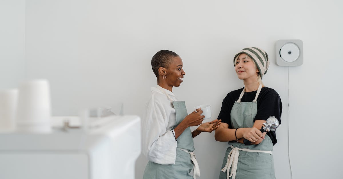 Can I drink stuff bought in duty-free shops onboard a plane? - Couple of multiracial female baristas wearing apron standing near wall in modern coffee shop with minimal interior while drinking coffee and communicating and looking at each other