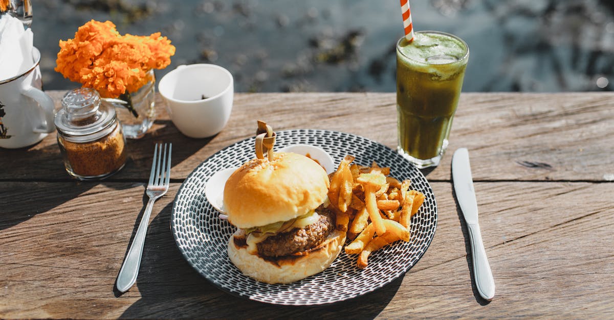 Can I eat a beef burger in India? - Plate with appetizing hamburger and french fries placed on lumber table near glass of green drink in outdoor cafe