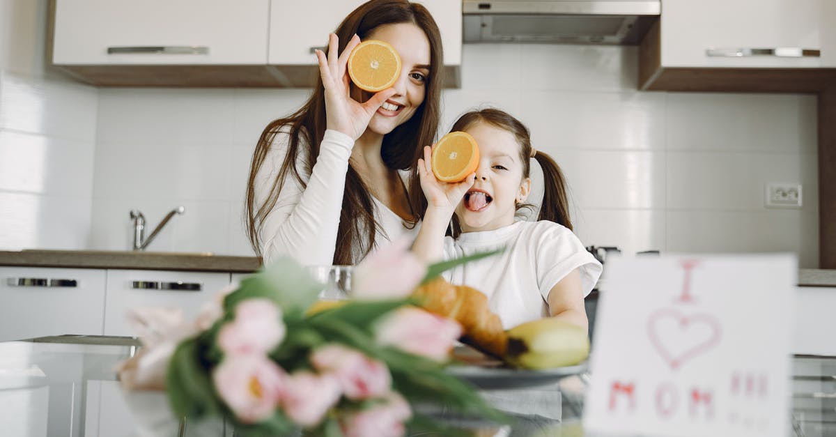 Can I eat only a crème brûlée in Paris? - From below of cheerful mother and daughter in domestic clothes smiling and playing with oranges while sitting together at table with bouquet of tulip and drawing of child