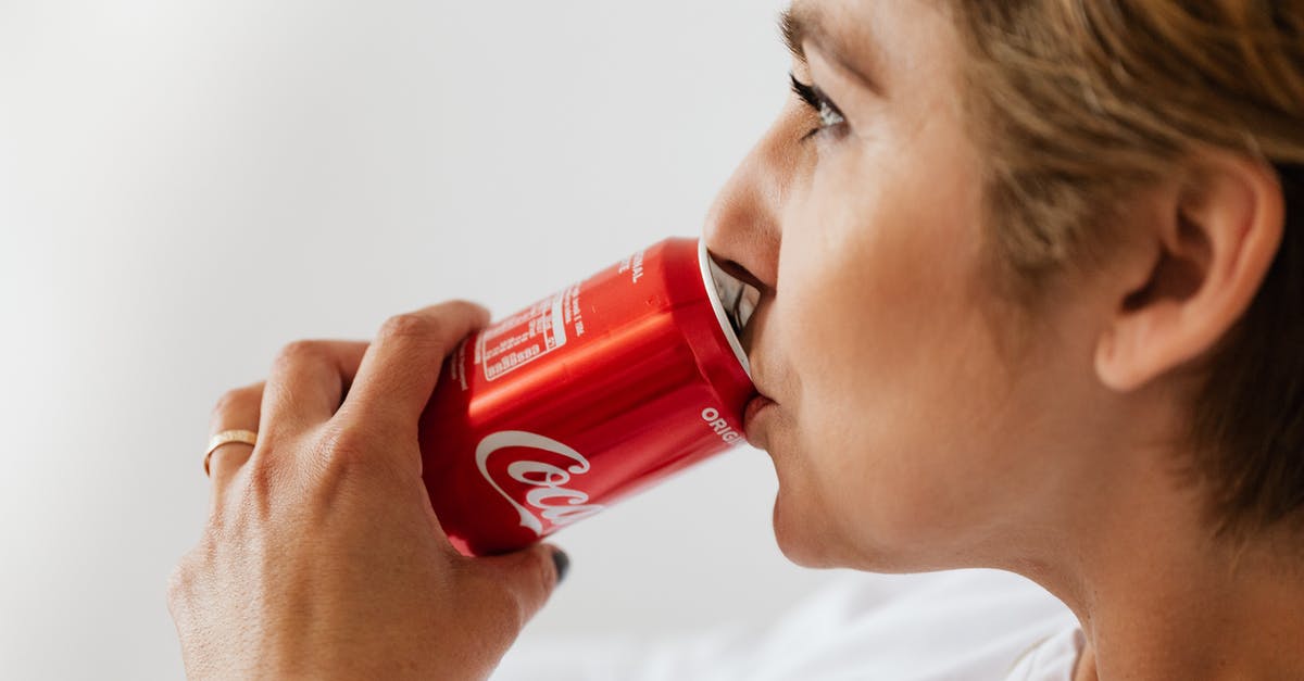 Can I fly with a gold bar? - Side view of crop wistful female in casual wear and gold ring enjoying coke from red can while sitting near white wall and looking away