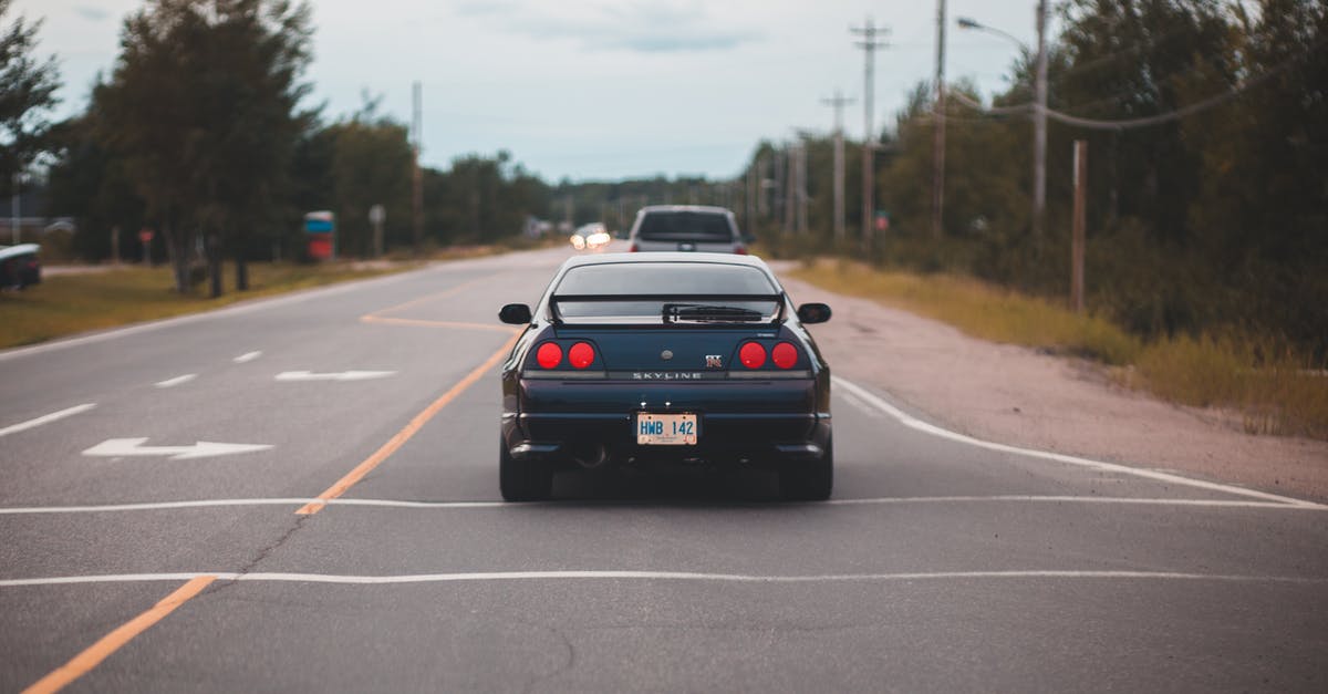 Can I get a driving license on a visitor visa? - Rear bumper of luxury automobile on asphalt roadway with arrows between greenery trees under cloudy sky