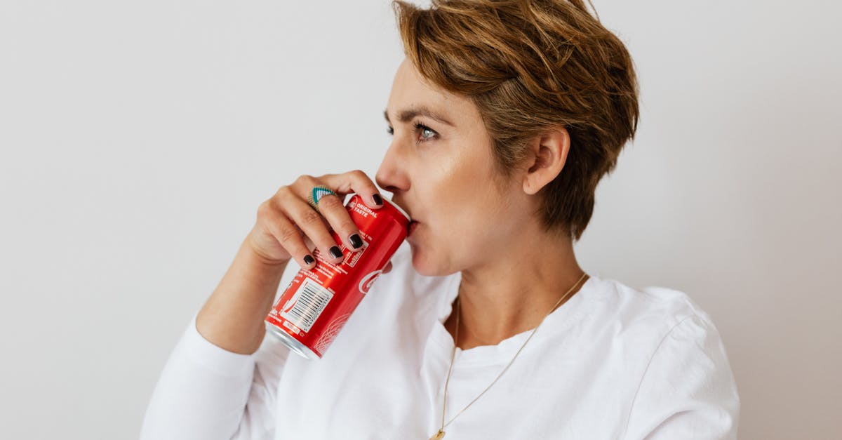 Can I get a UK Visa at short notice? - Pensive female in white wear with gold necklace and ring on finger drinking cold coke from red can and looking away