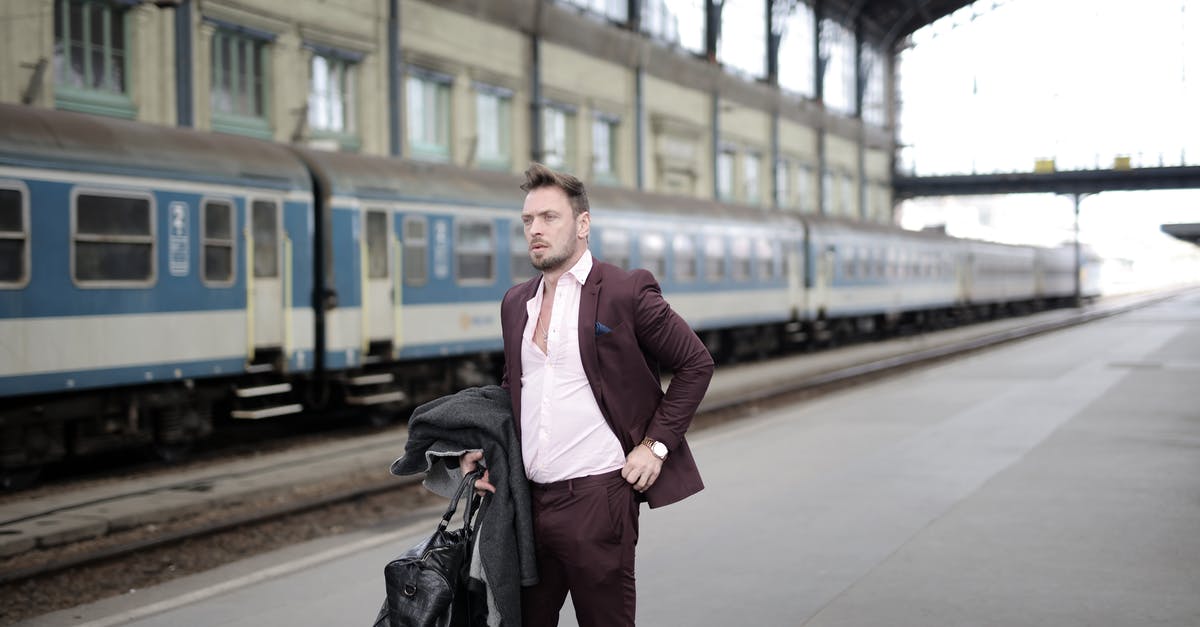 Can I get off the train or discontinue my journey before reaching the destination station? - Serious stylish businessman in elegant white shirt and purple jacket holding leather bag and coat in hand standing on platform on railway station and waiting for train