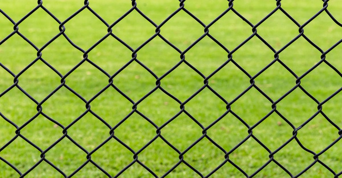 Can I get through a ticket barrier if I didn’t put my ticket through at the start of the journey? - Full frame background of fence with chain link net on blurred green meadow