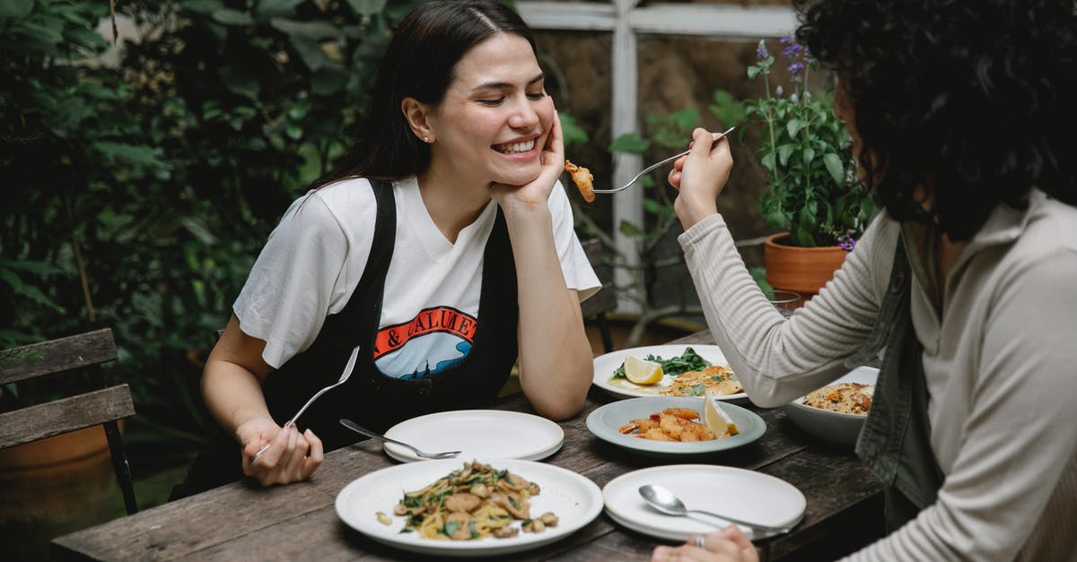 Can I give luggage to friend during transit? - Female giving food on fork to cheerful friend while having lunch in outdoor terrace