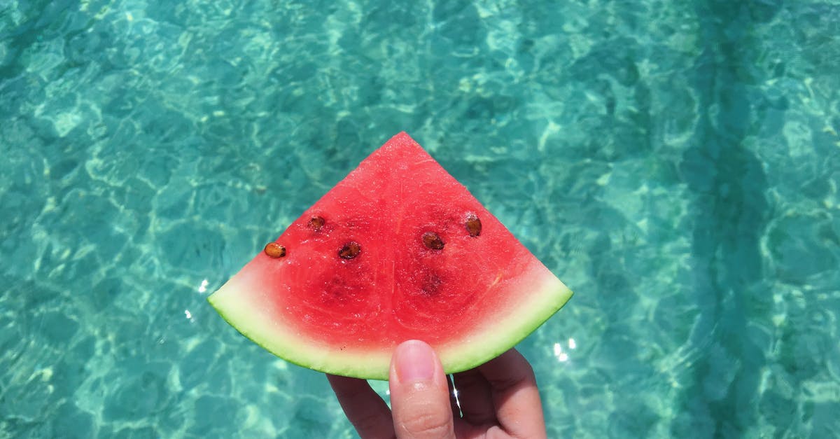 Can I have a watermelon in hand luggage? - Hand Holding a Slice of Watermelon With Blue Swimming Pool Water in the Background