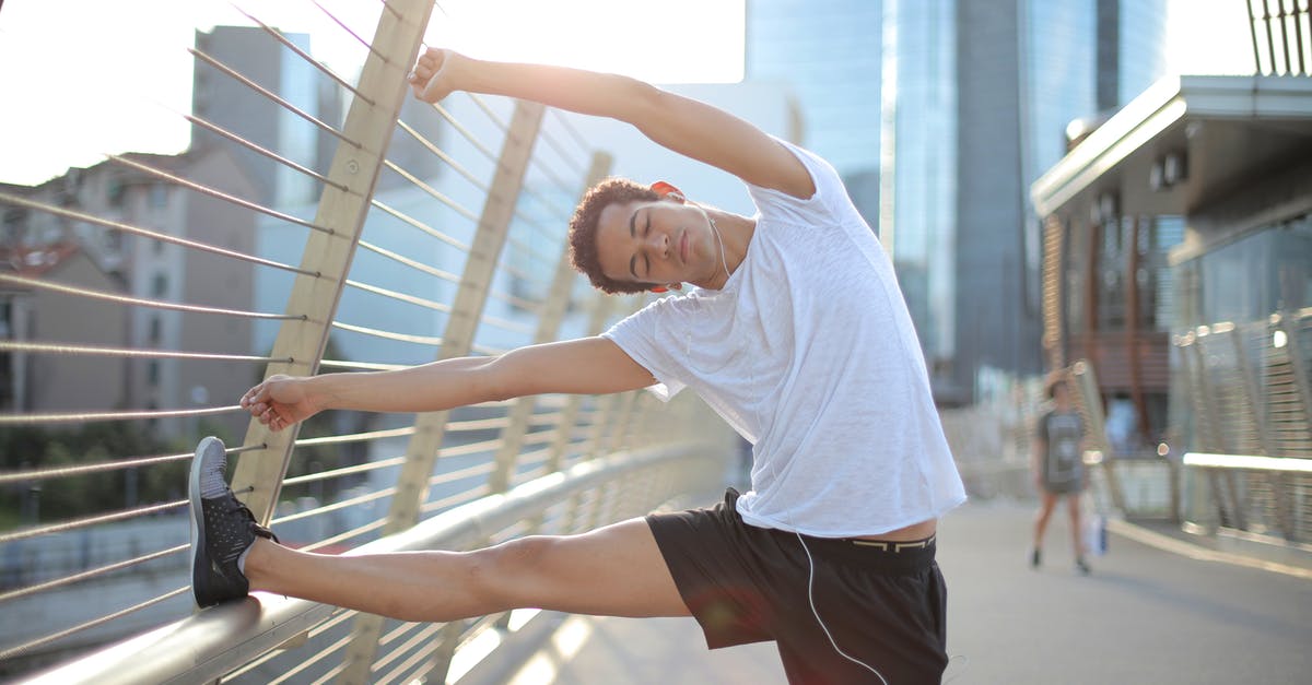 Can I have the final leg of a multi-city flight refunded? - Calm focused  African American male athlete with eyes closed in earphones and sportswear leaning on metal fence and doing side bend exercise while listening to music and stretching body on street against blurred urban environment in sunny day