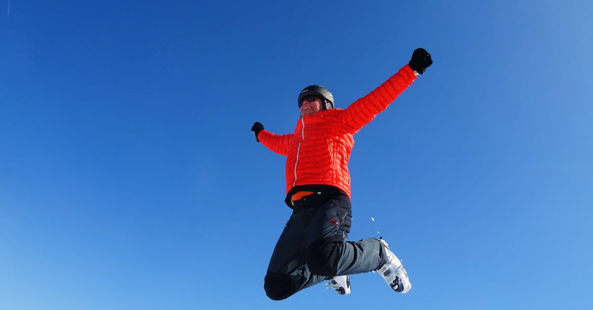 Can I learn ski jumping in Japan? - Man in Orange Zip Jacket and Black Pants Jumping Under Blue Sunny Sky