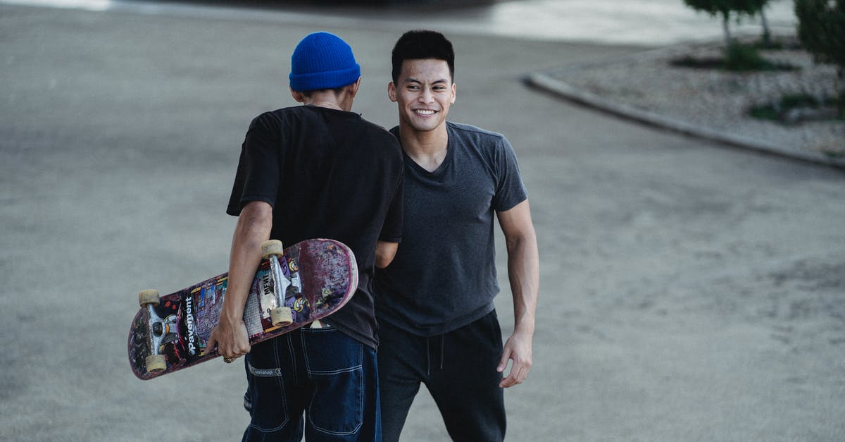 Can I meet my friend during a connecting flight? (LHR) - Cheerful young Asian men in casual clothes bumping shoulders and smiling while greeting each other on street