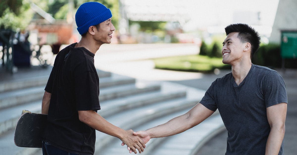 Can I meet my friend during a connecting flight? (LHR) - Cheerful young Asian men in street wear shaking hands and greeting each other with friendly smile