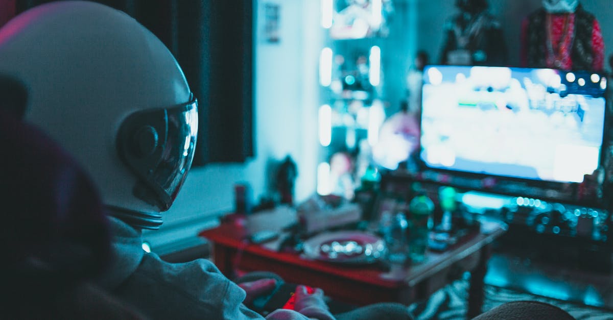 Can I play erotic video games (digital version) in the UAE? - Side view of unrecognizable person in virtual reality helmet sitting on sofa and playing with gamepad in dark room