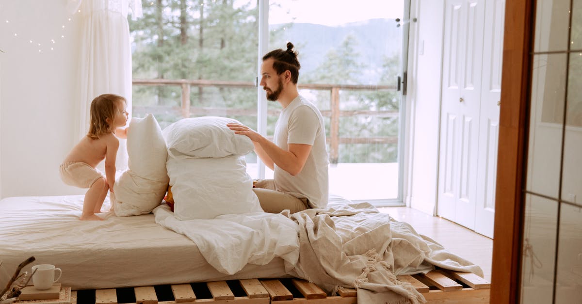 Can I put a bed quilt/blanket in airplane's cargo? - Side view of serious bearded father in casual clothes playing with little child with pillows on comfortable bed in light bedroom at home