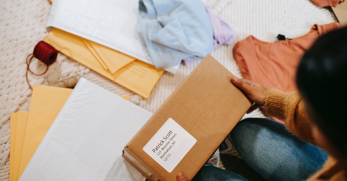 Can I receive a parcel in Norway without an address? - Top view of crop anonymous female with carton box of parcel checking address among envelopes