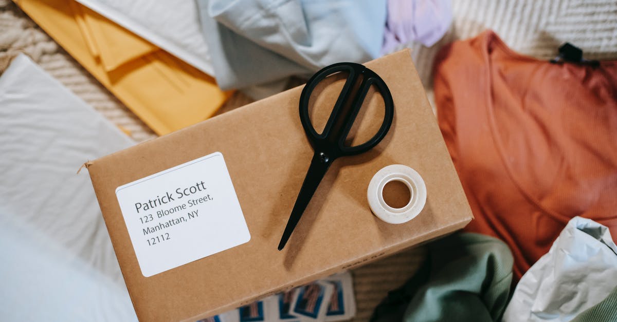 Can I receive a parcel in Norway without an address? - Top view of tape with scissors on carton box with exact address and name among clothes