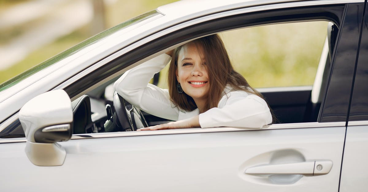 Can I rent a car in Berlin and drive to Krakow? - Cheerful female driver in white shirt sitting inside modern automobile and looking at camera through opened side window with smile during car trip in summer day