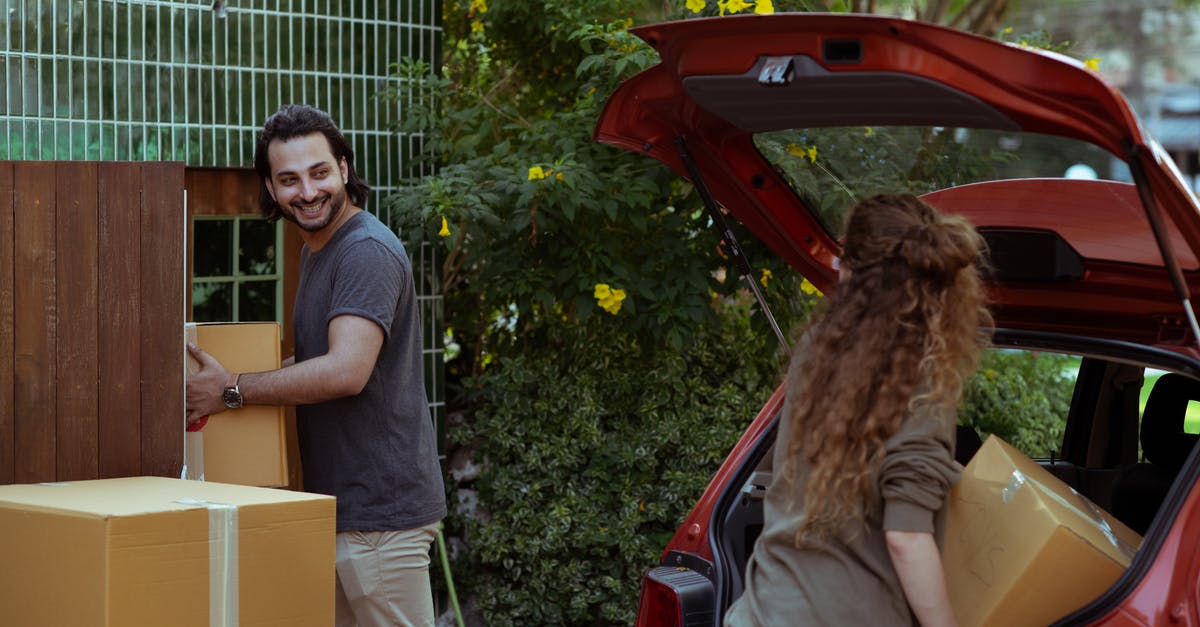 Can I rent a car in Paris without a credit card? - Happy couple in casual clothes moving personal items in carton boxes from car trunk to new house