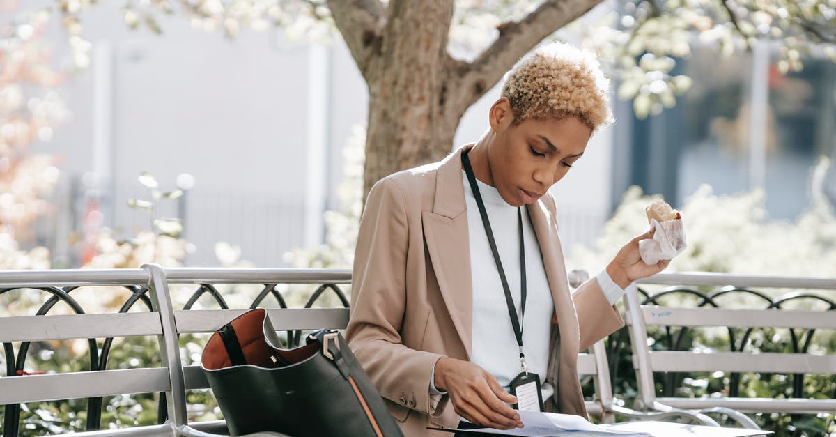 Can I safely eat whatever goes through the x-ray machine? - Pensive young African American female student in stylish jacket reading documents in folder and eating sandwich sitting in park