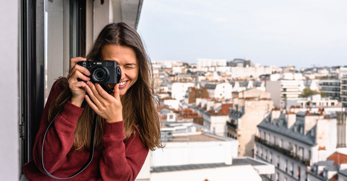 Can I sell the photographs I take on a tourist visa? - Woman Wearing Maroon Sweater Standing on Veranda Using Camera While Smiling Overlooking Houses and Buildings