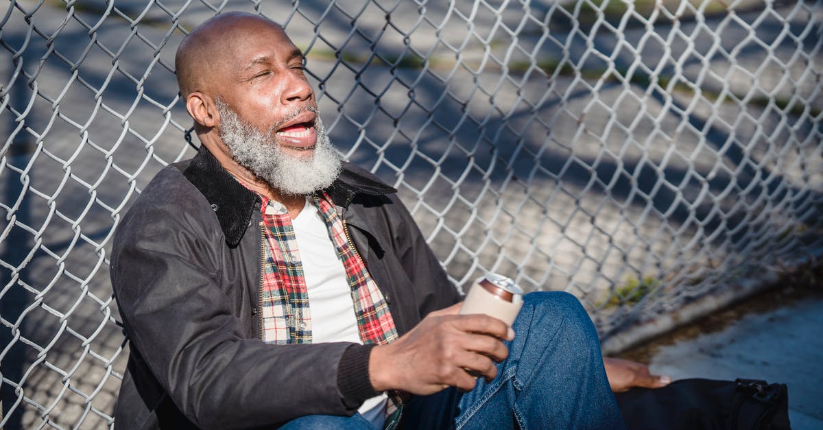 Can I sleep on a airplane tray table? - African American senior man with closed eyes and opened mouth sitting near metal fence and holding beer can