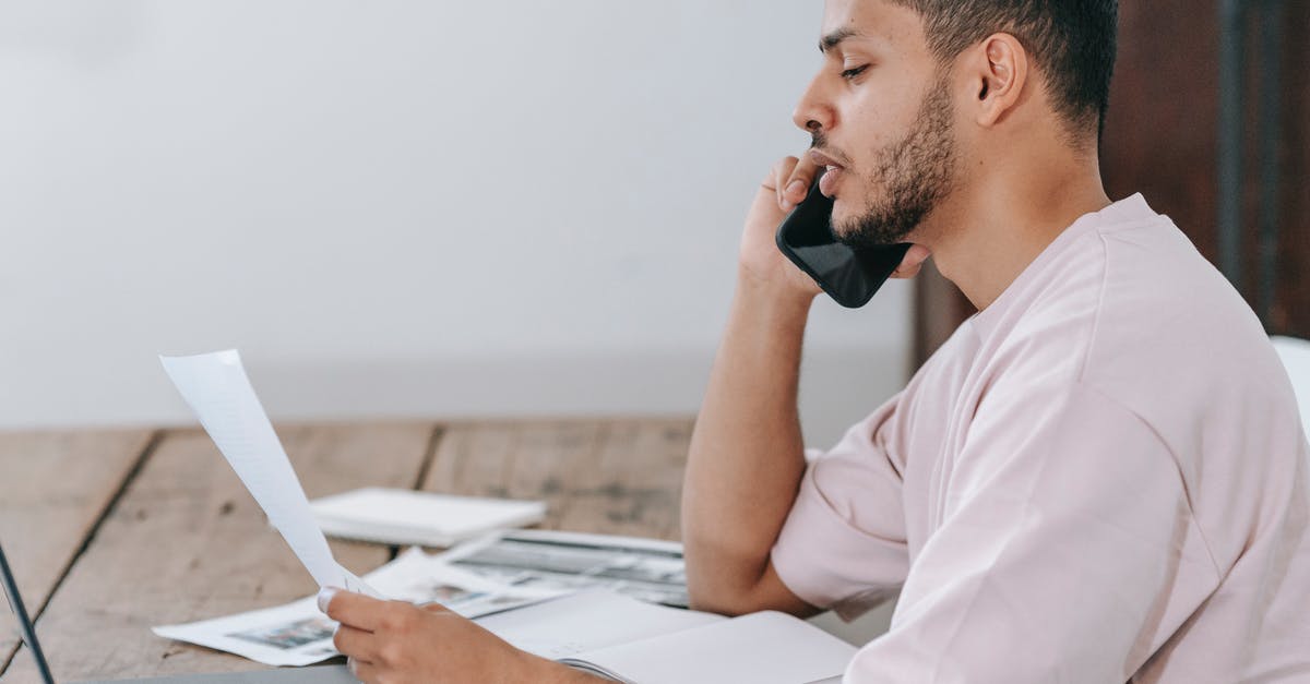 Can I submit Job offer letter as proof of employment? - Side view of young Hispanic male remote employee discussing documents during phone call while working online with laptop and papers in home office