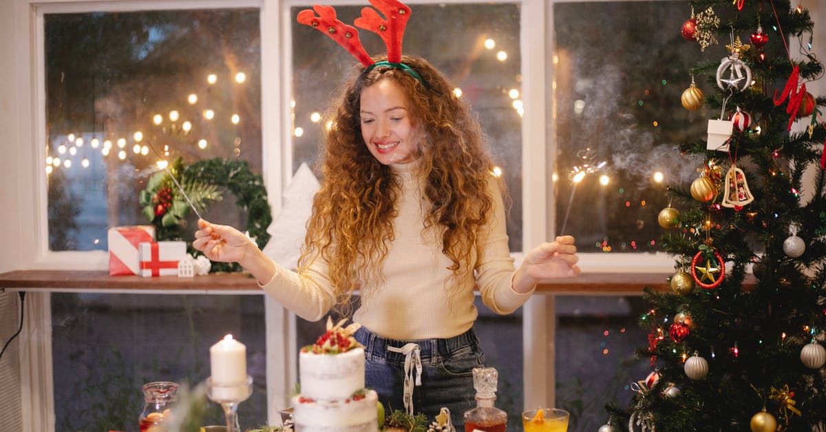 Can I take a home baked christmas cake into Australia? - Cheerful female in decorative deer horns with burning sparklers standing at table with tasty cake for New Year holiday at home