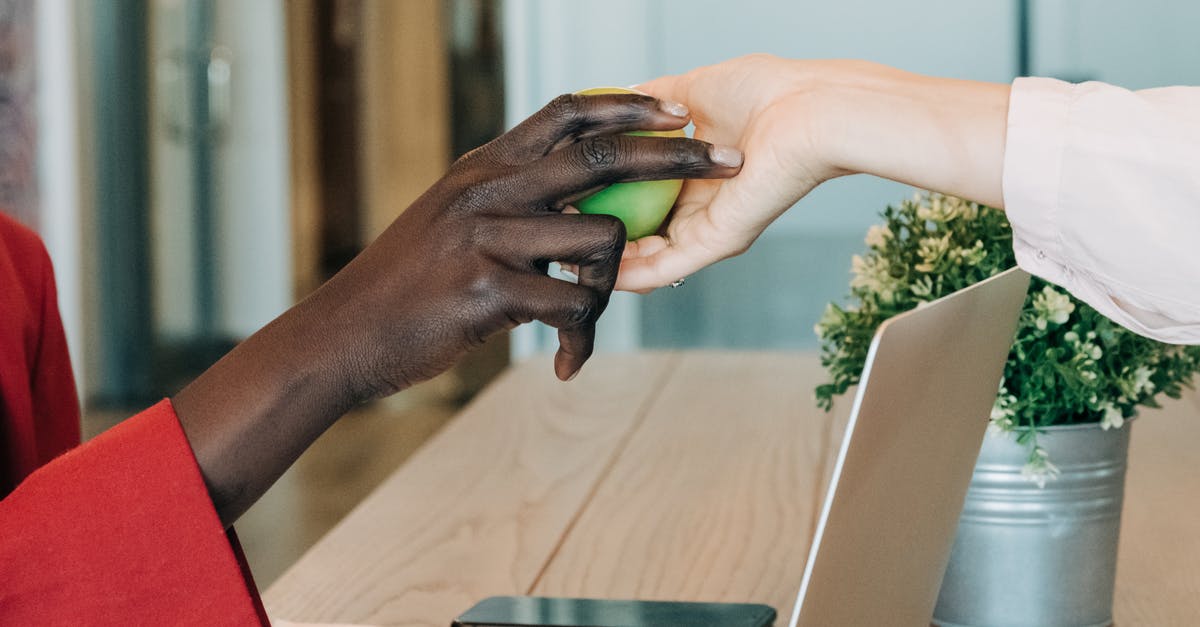 Can I take a laptop into Japan? - Black businesswoman taking green apple from colleague at workplace