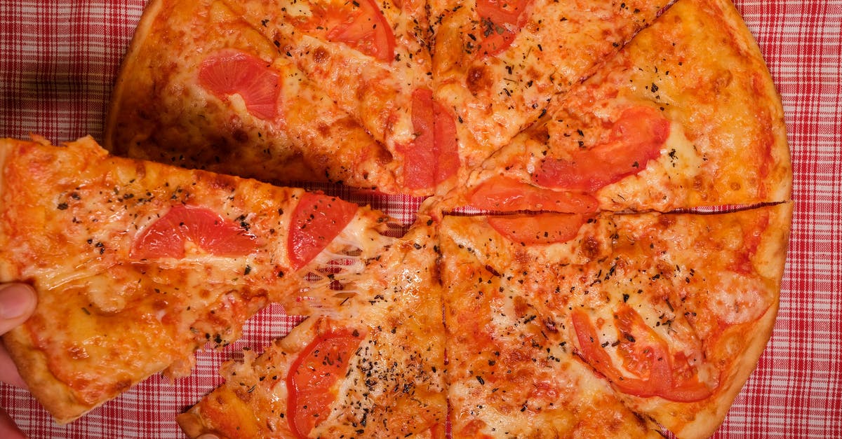 Can I take an extra piece of luggage to the USA? - Top view of crop anonymous person taking slice of yummy pizza with tomato and oregano placed on checkered tablecloth