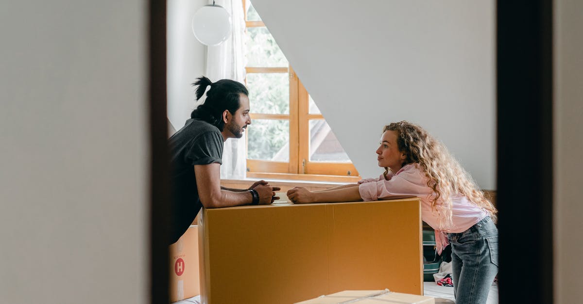 Can I take beef jerky in my carry-on? - Side view from entrance of cheerful young ethnic bearded man with ponytail and woman with curly hair leaning on large cardboard package while arranging stuff in cozy attic bedroom