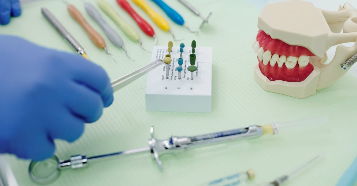 Can I take orthodontic wires in my hand luggage? - From above of crop faceless orthodontist in latex gloves and tweezers working at medical table with cast jaw and set of syringes near periodontal scalers