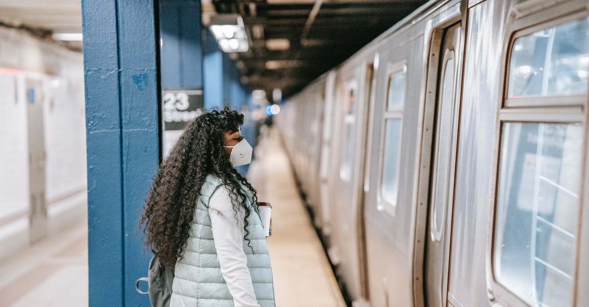 Can I transit in the US with my student visa? - Side view of young African American female student in casual clothes and protecting mask standing on platform of metro station with backpack in front of train