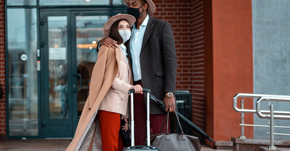 Can I travel while waiting for my new passport? - Man and Woman With Face Masks Waiting Outside A Building 