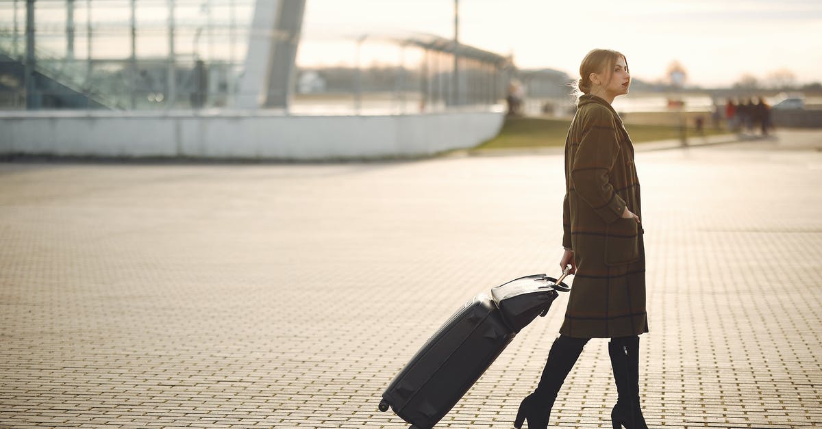 Can I travel with a suitcase full of condoms? - Side view of full length young female traveler in trendy plaid brown coat and high boots with suitcase walking on pavement near modern building on city street in morning