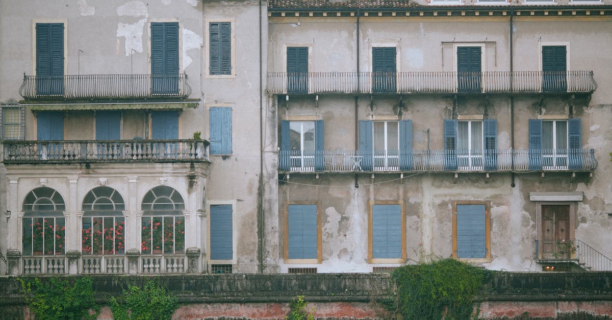 Can I travel within the Schengen area while my Italian residency card is being renewed? - Shabby old building decorated and windows with balconies and fence with green plants in city in daytime