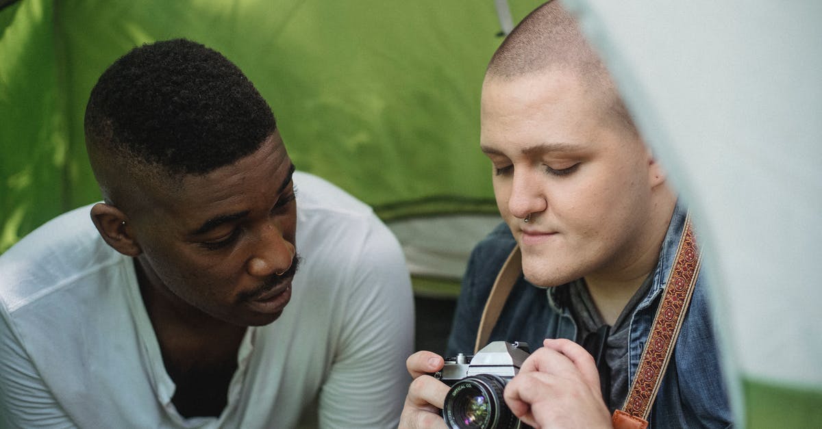 Can I use a bike-sharing in Germany as a traveler? - Young male showing sharing retro photo camera with African American friend while sitting in green tent