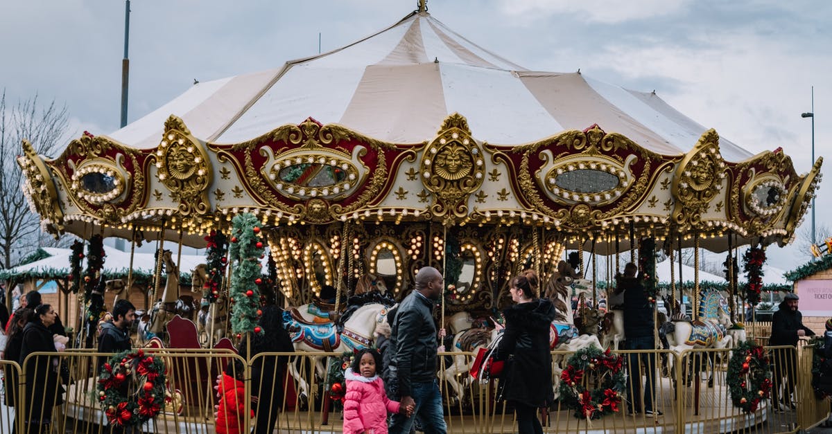 Can I visit my father in the USA? - Side view of black father with girl passing by glowing carousel in city fairground on gloomy day