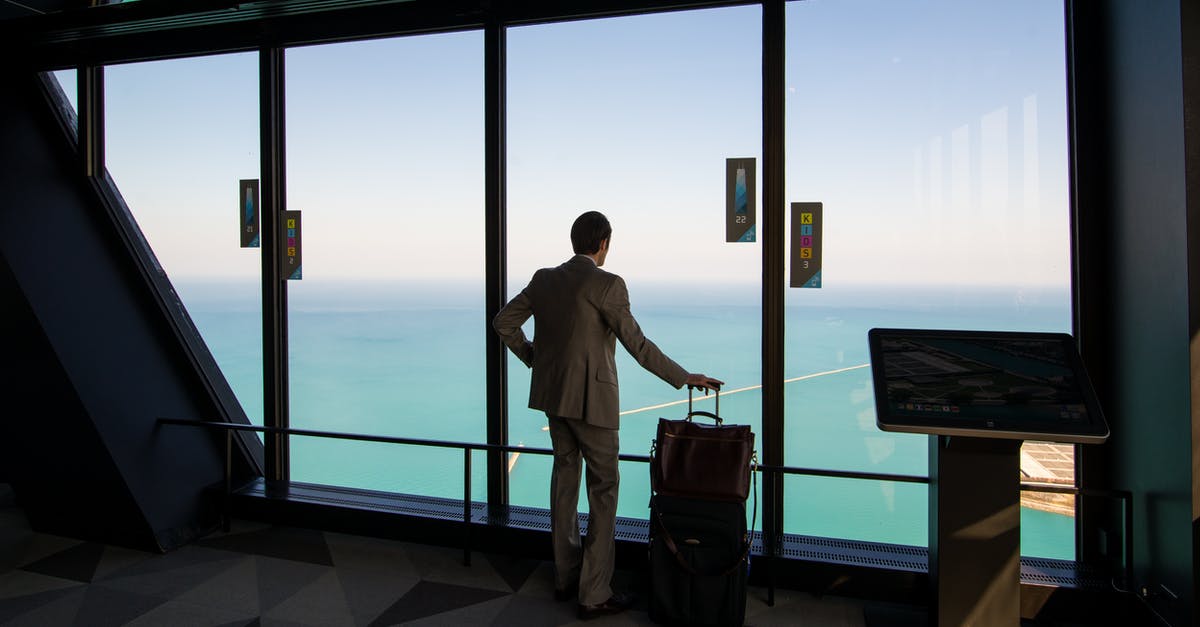 Can Israelis recheck luggage in Dubai? - Man in White Dress Shirt and Blue Denim Jeans Standing Near Glass Window