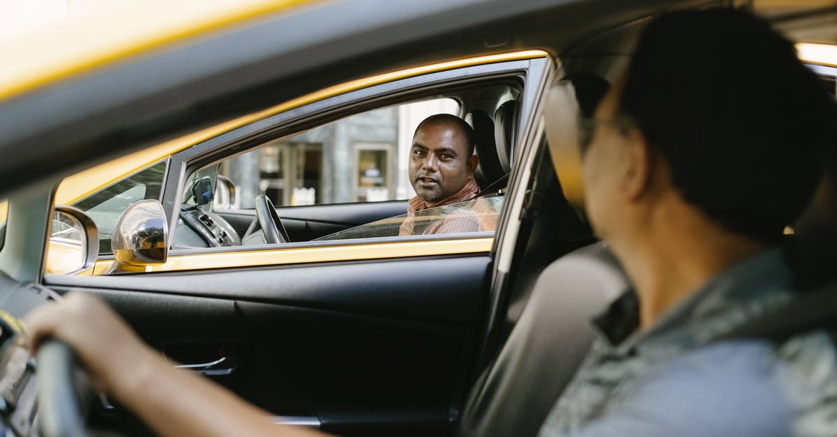 Can my friend legally drive my car in Canada? - Side view of adult ethnic male cab driver interacting with anonymous colleague driving auto while looking at each other in city