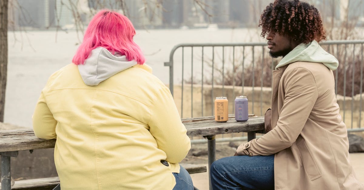 Can you drink tap water in Spain? - Stylish African American man and faceless woman with pink hair sitting at wooden table with cans of drinks while spending time on waterfront