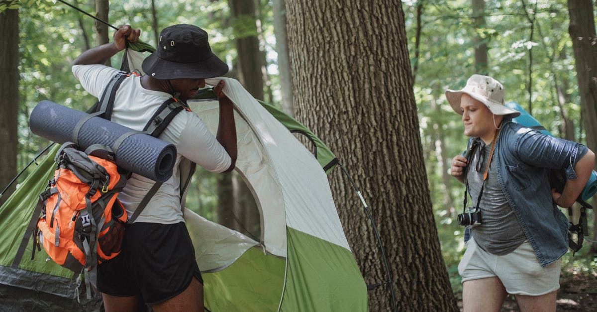 Can you freely camp along trails in Scotland? - Traveling men in shorts and hats setting up camping tent in woods