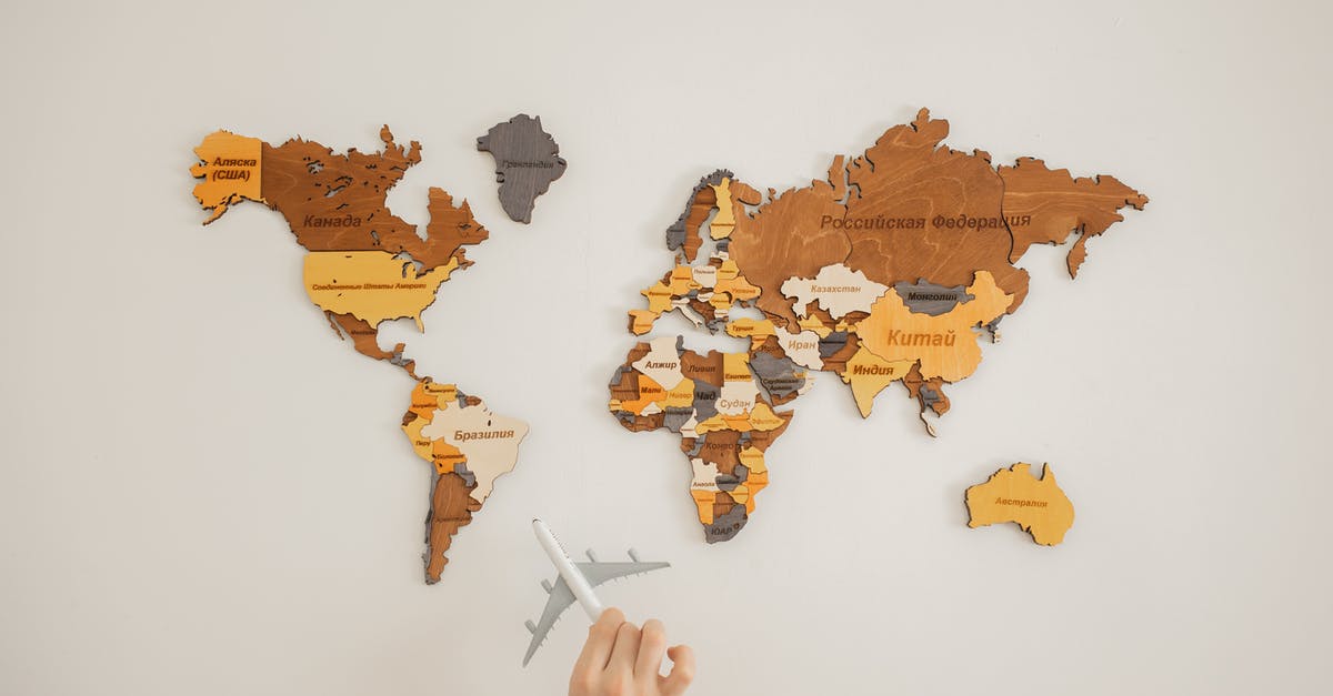 Can you name those countries on Schengen visa? - Crop unrecognizable person with toy aircraft near multicolored decorative world map with continents attached on white background in light studio