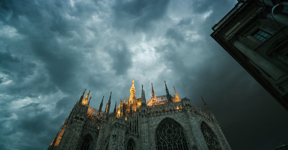 Can you see Putin in Duomo di Milano? - Low angle of Metropolitan Cathedral Basilica of Nativity of Saint Mary in Milan with sharp spires lit up with bright light against gloomy overcast sky