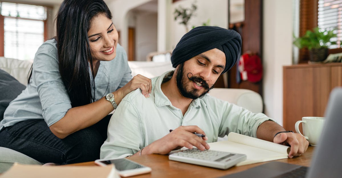 Can you work online with an Indian Tourist Visa? - Smiling young Indian female in casual clothes supporting husband during remote work at home sitting in front of laptop with calculator notebook smartphone and cup of coffee at table